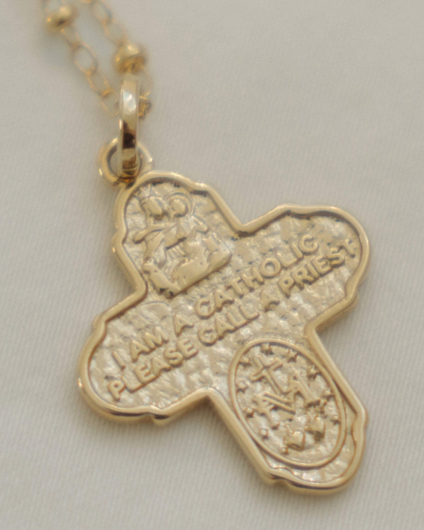 Gold cross pendant with engraved text on a light gray background.