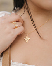 Close-up of a person wearing a gold four way cross necklace and catholic gold rings.