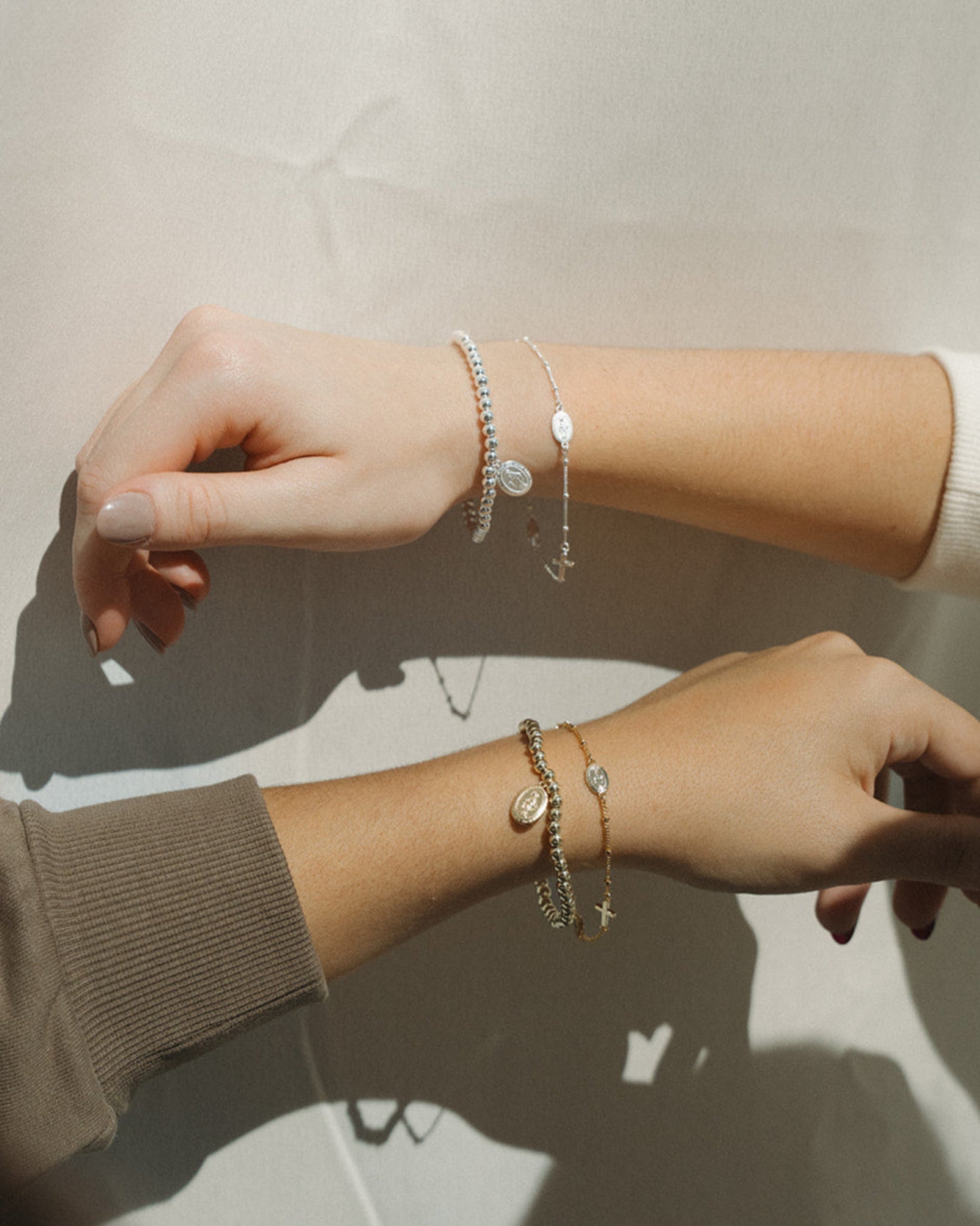 Close-up of a person's wrist with multiple Catholic rosary bracelets on a neutral background