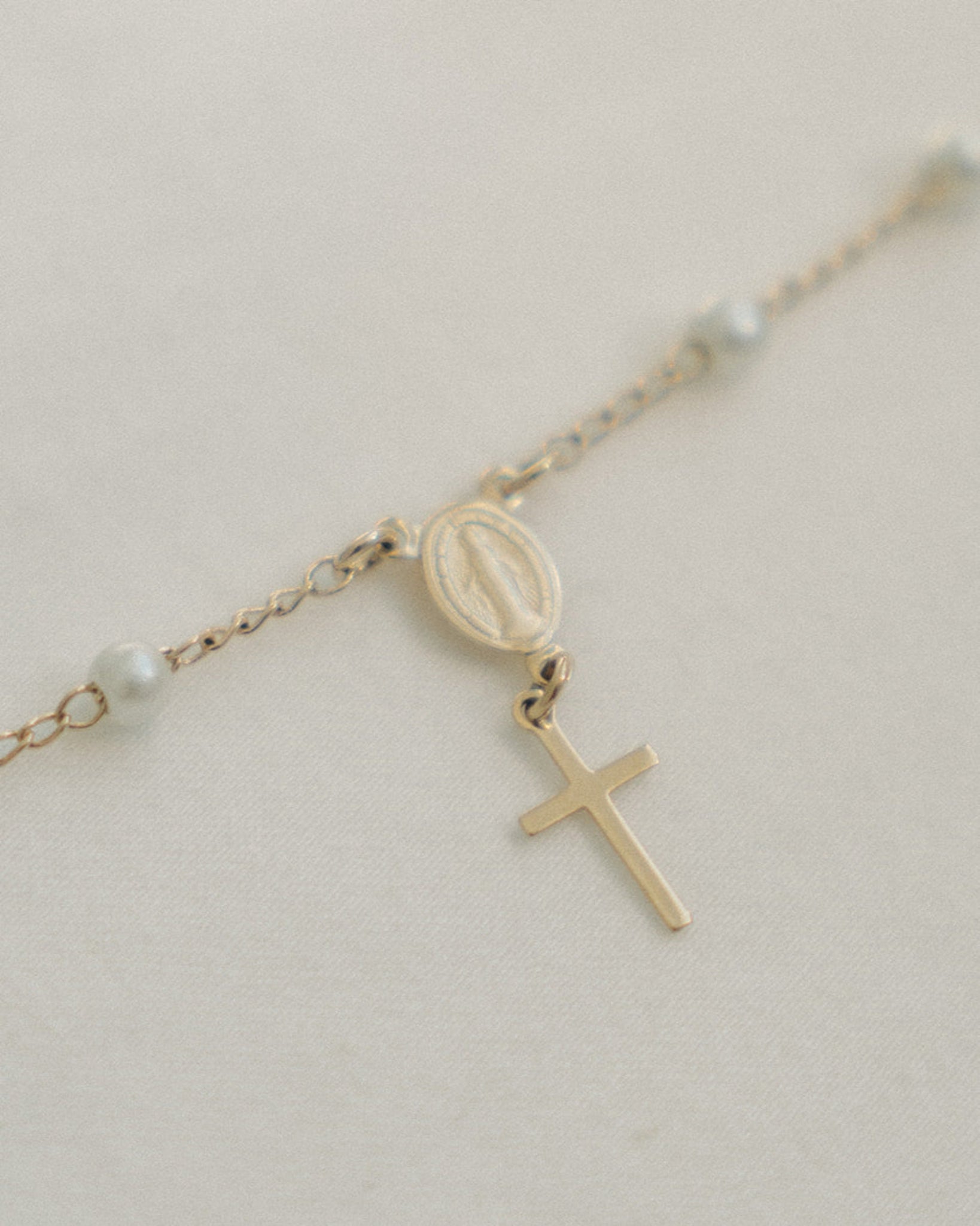 Gold pearl rosary bracelet with a cross pendant on a light background