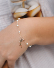 Pearl rosary bracelet with a cross charm on a wrist against a neutral background
