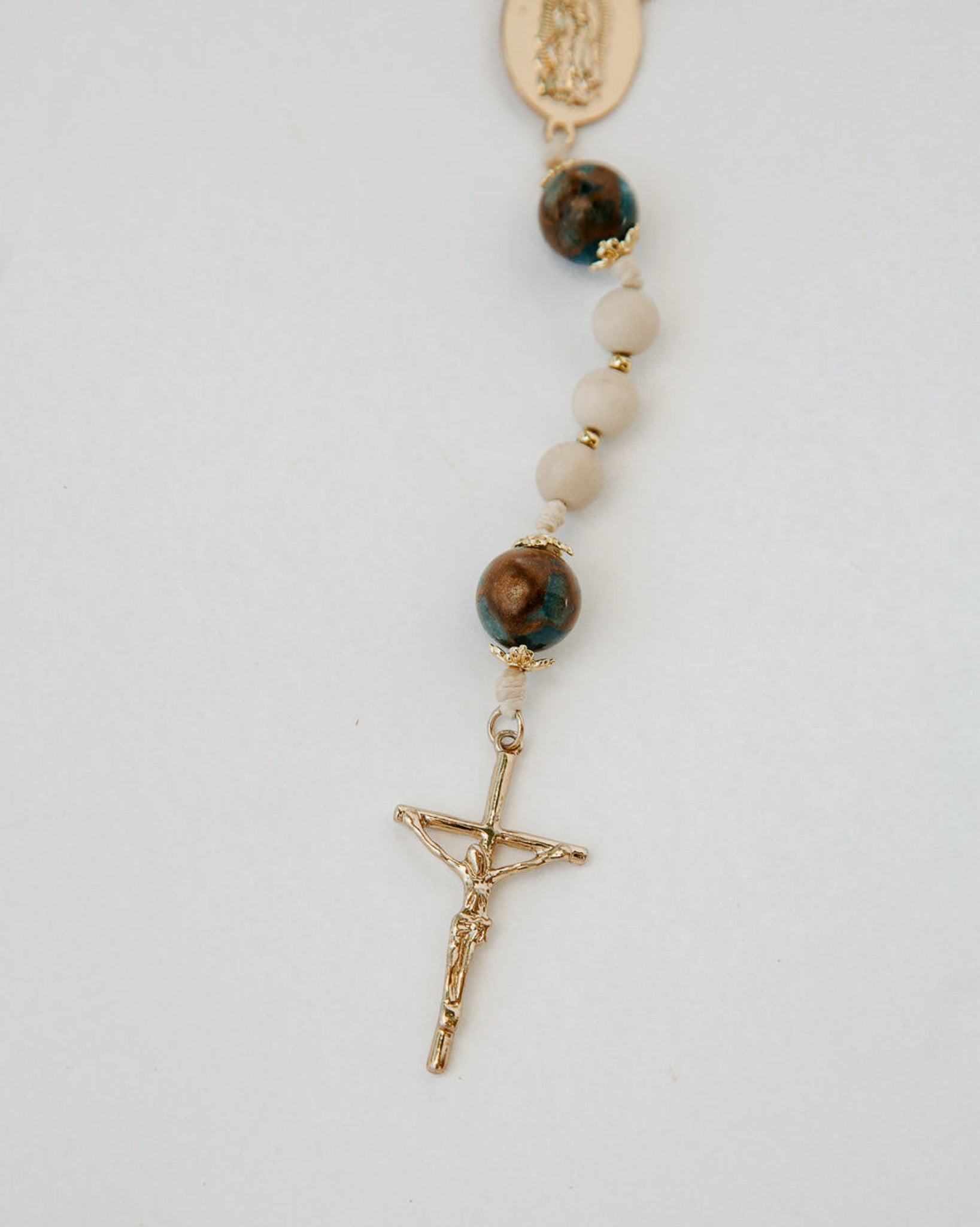 Rosary with stone beads and gold crucifix on a white background