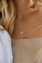 A close-up lifestyle shot of a woman wearing a delicate gold chain necklace with a small, sacred heart pendent. She is wearing a beige linen top.