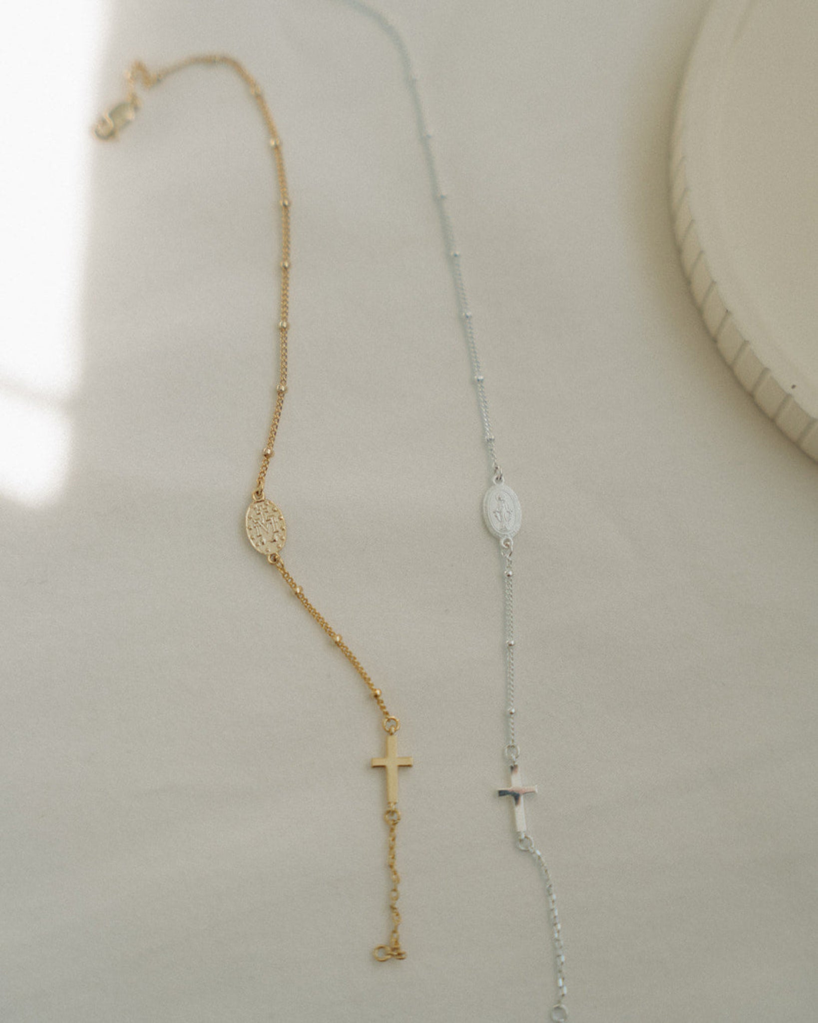 Gold and silver rosary bracelets on a light beige background