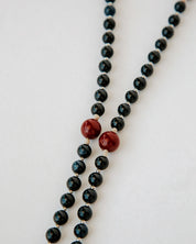 Rosary with black beads and red accents on a white background