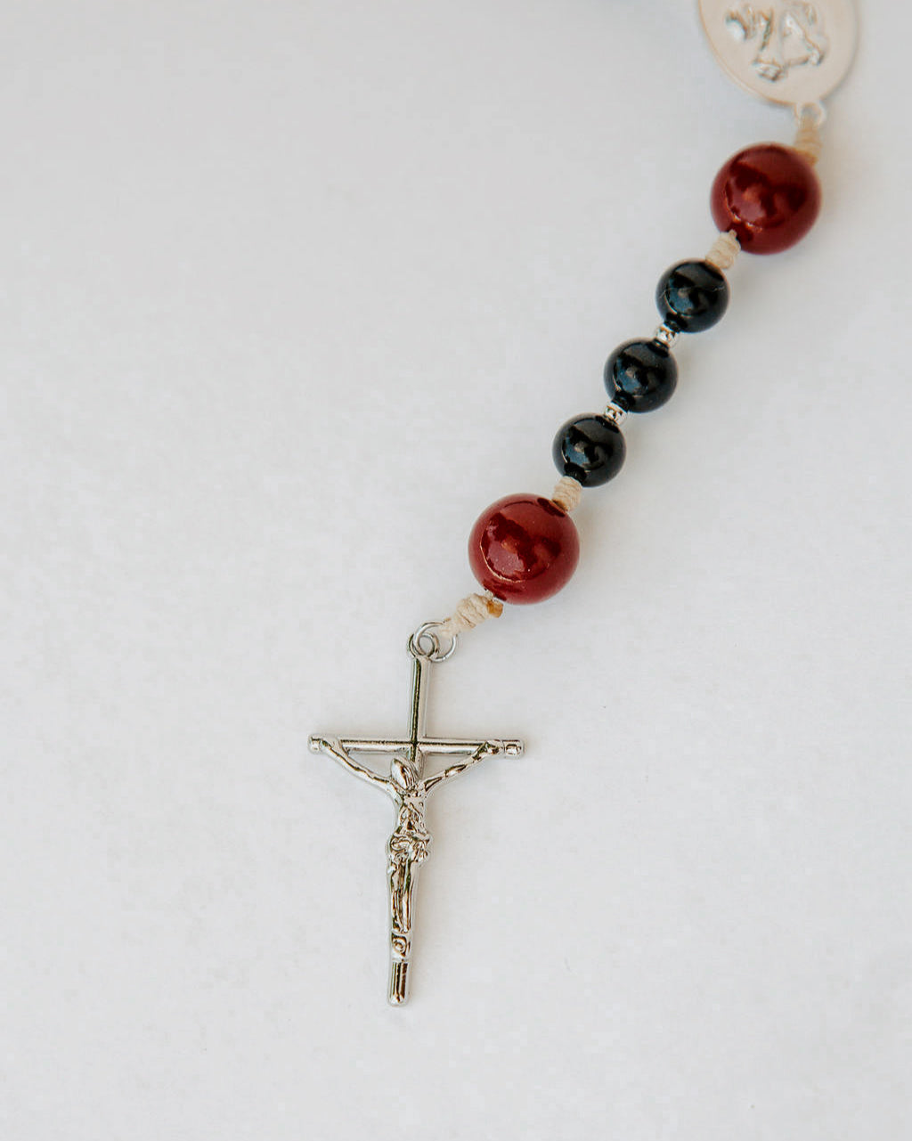 Rosary with red and black beads with a silver cross on a white background 
