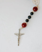 Rosary with red and black beads with a silver cross on a white background 