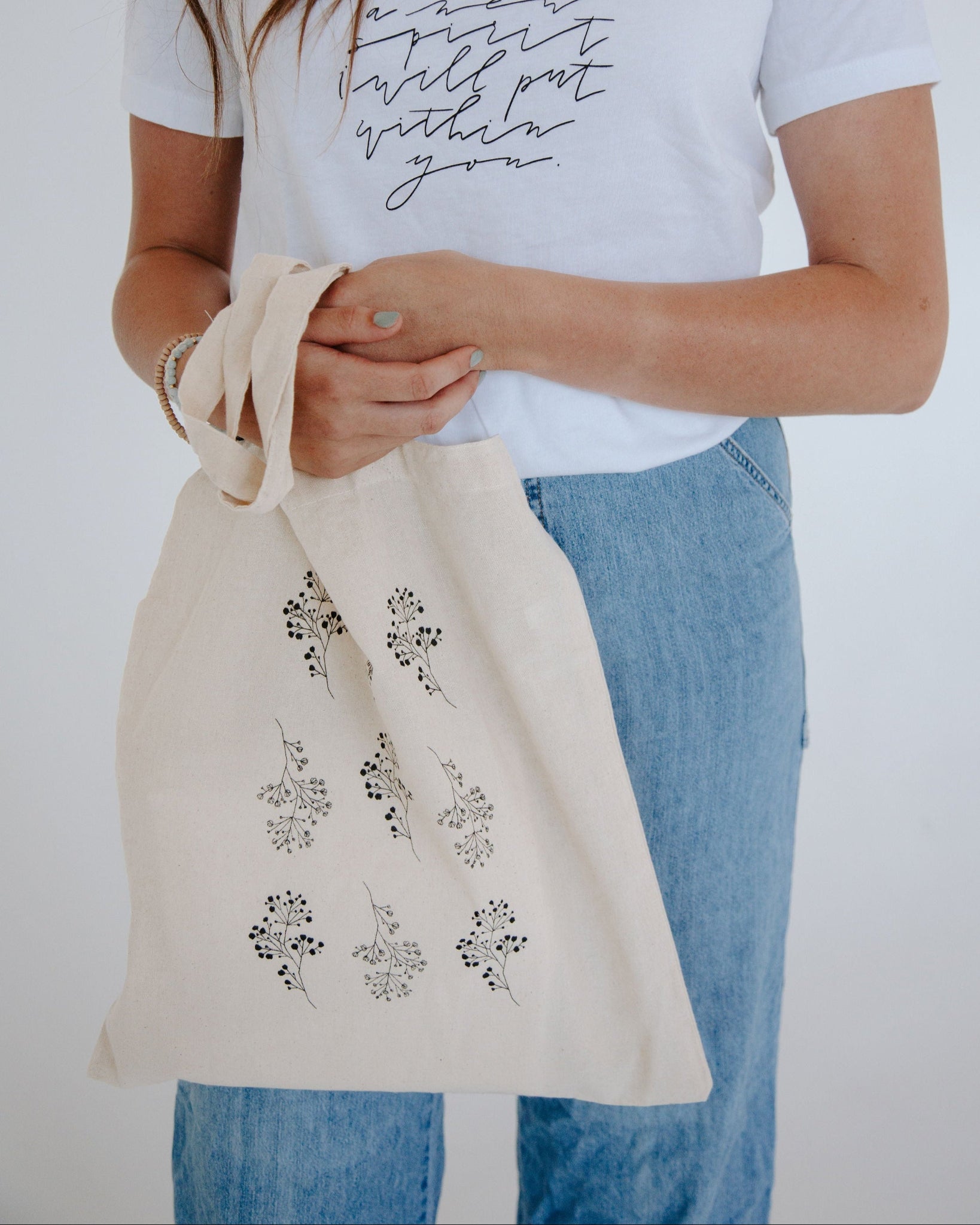 Person holding a tote bag with floral designs against a plain background