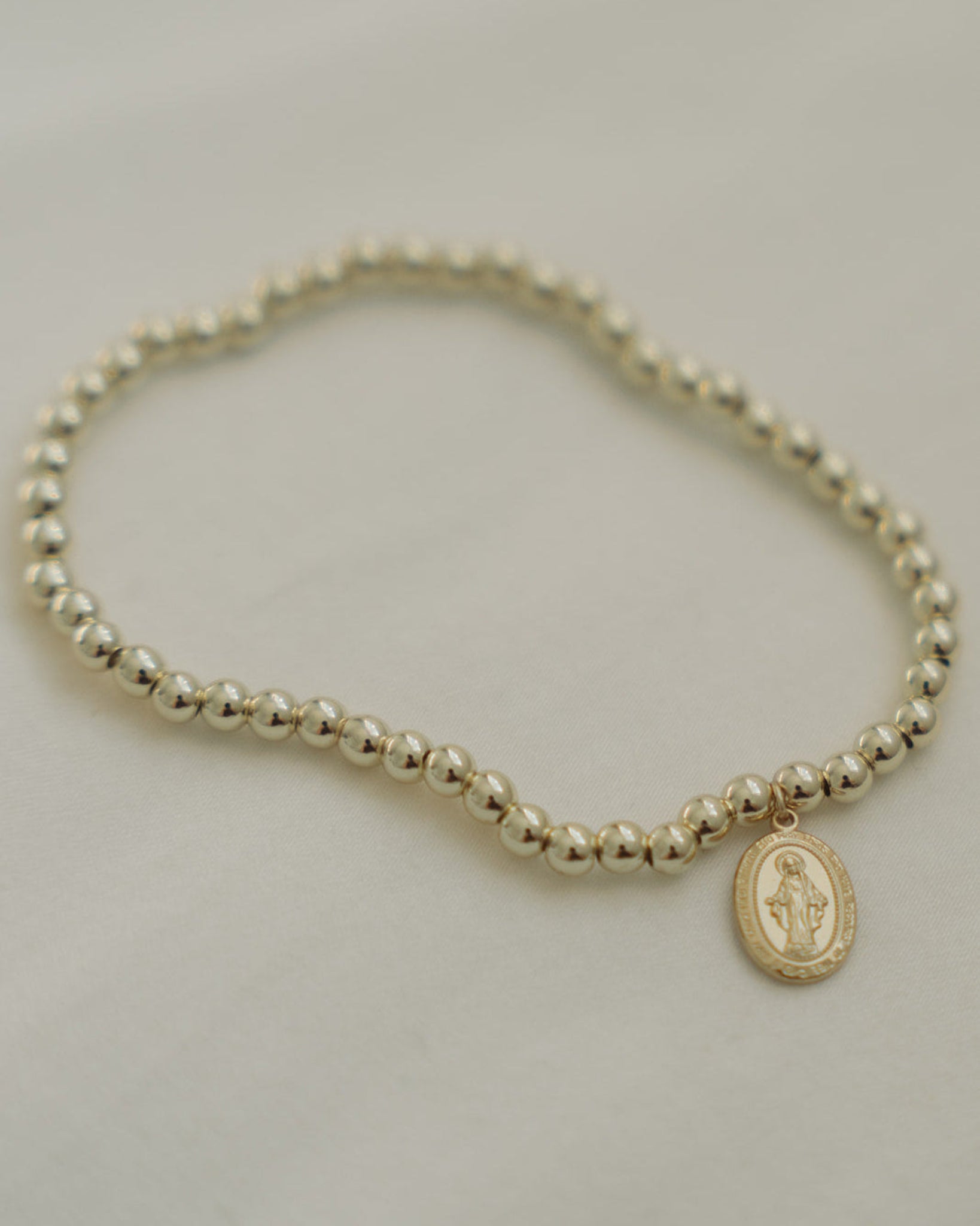 Gold beaded Miraculous Medal bracelet on a light gray background