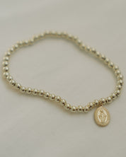 Gold beaded Miraculous Medal bracelet on a light gray background