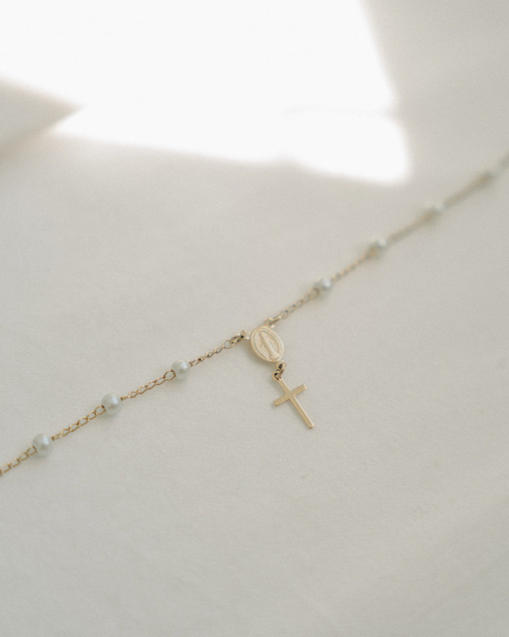 Delicate gold rosary bracelet with a cross on a light background