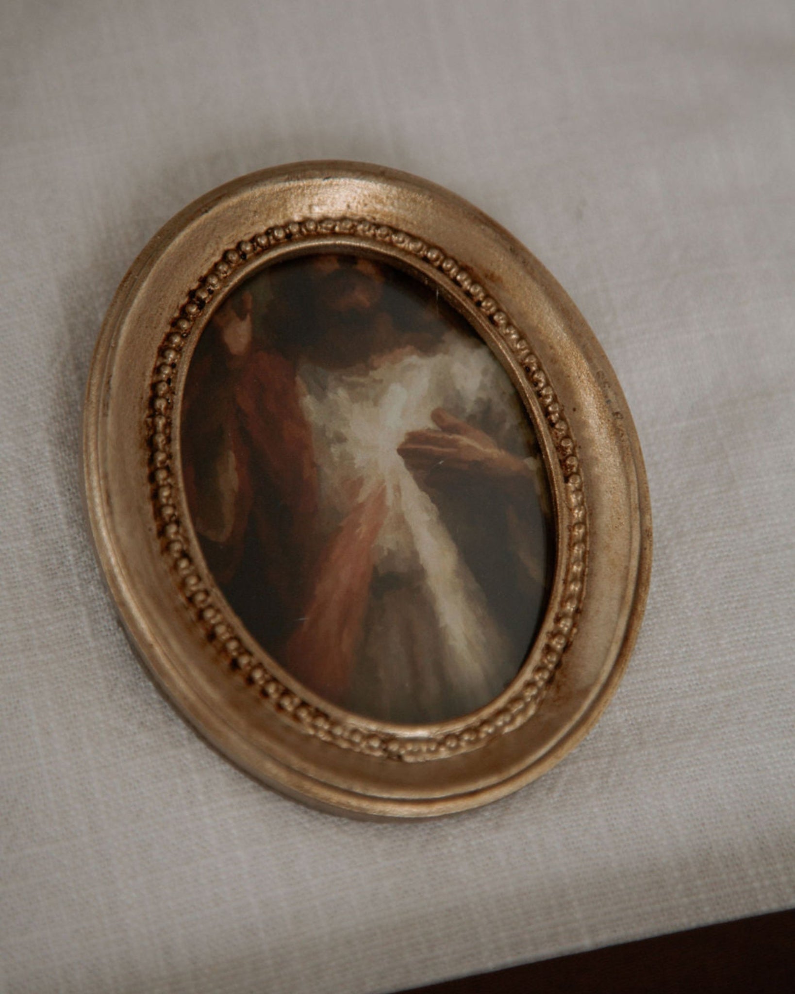 Small oval painting of divine mercy in a gold frame on a textured beige surface