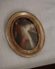 Small oval painting of divine mercy in a gold frame on a textured beige surface
