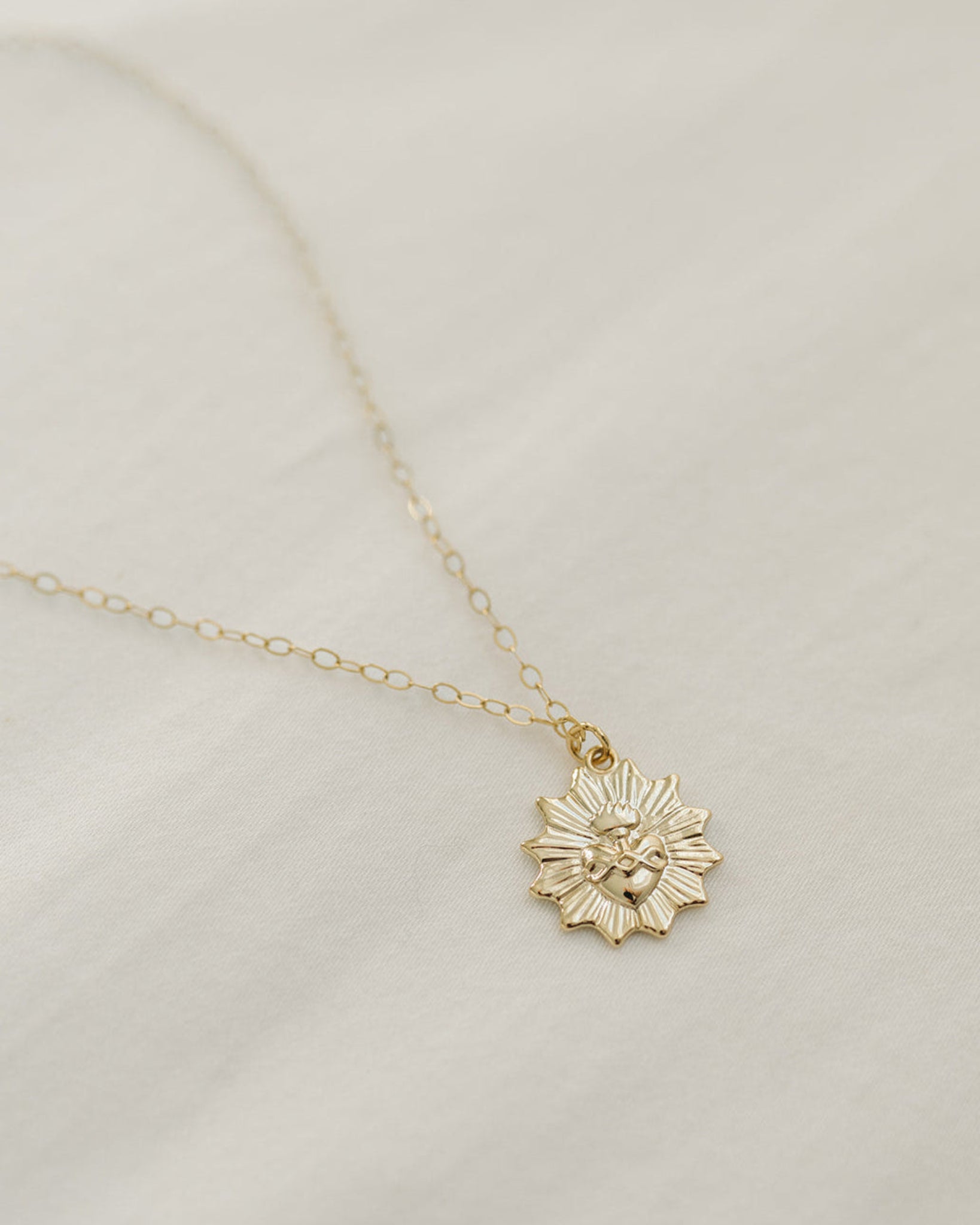 Gold necklace with a sacred heart pendant on a light beige background