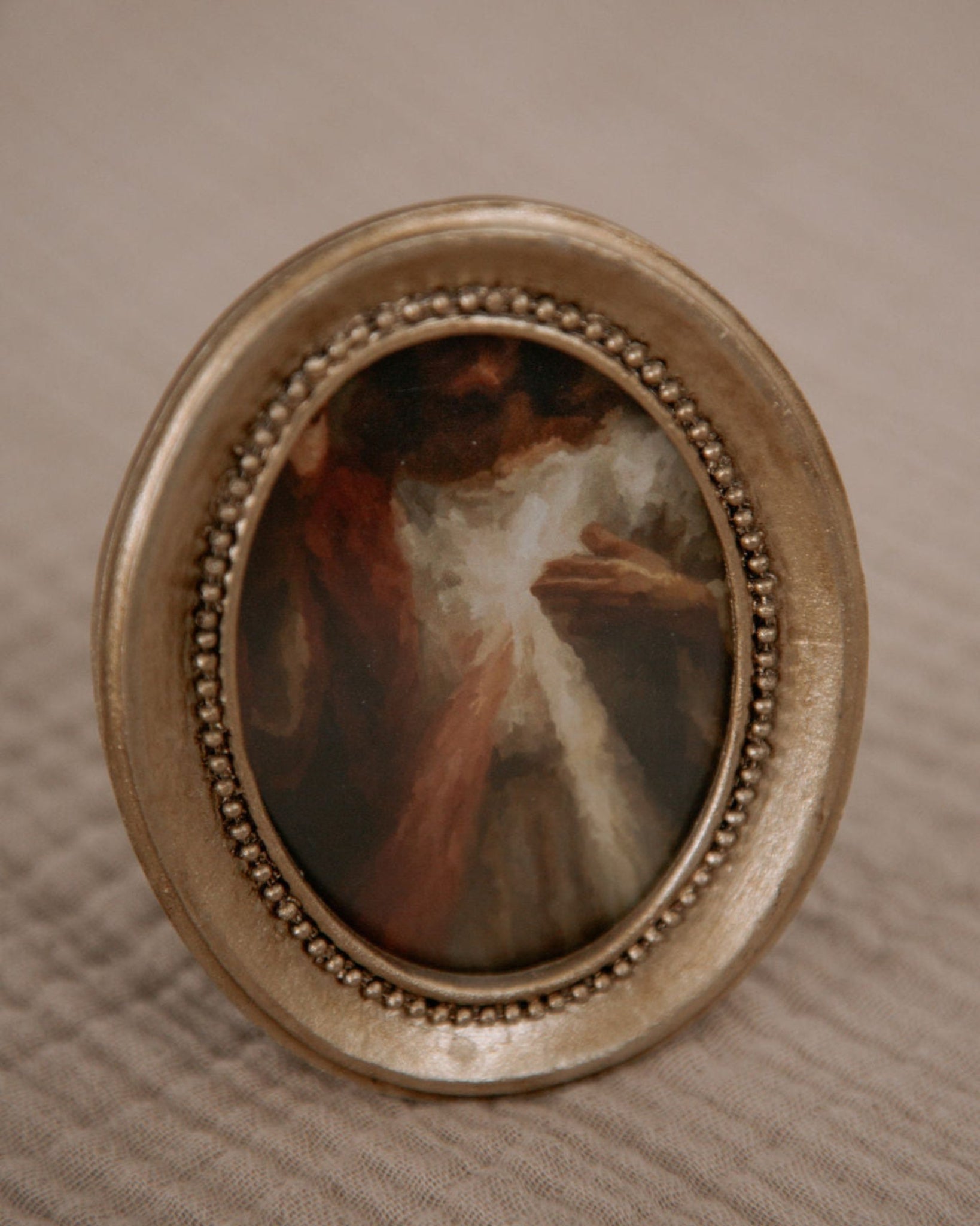 Catholic home decor in a small oval painting of the divine mercy image in a decorative gold frame on a textured beige surface