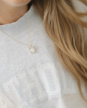 Person wearing a gray sweatshirt with 'CATHOLIC' text and a gold necklace with a square pendant.