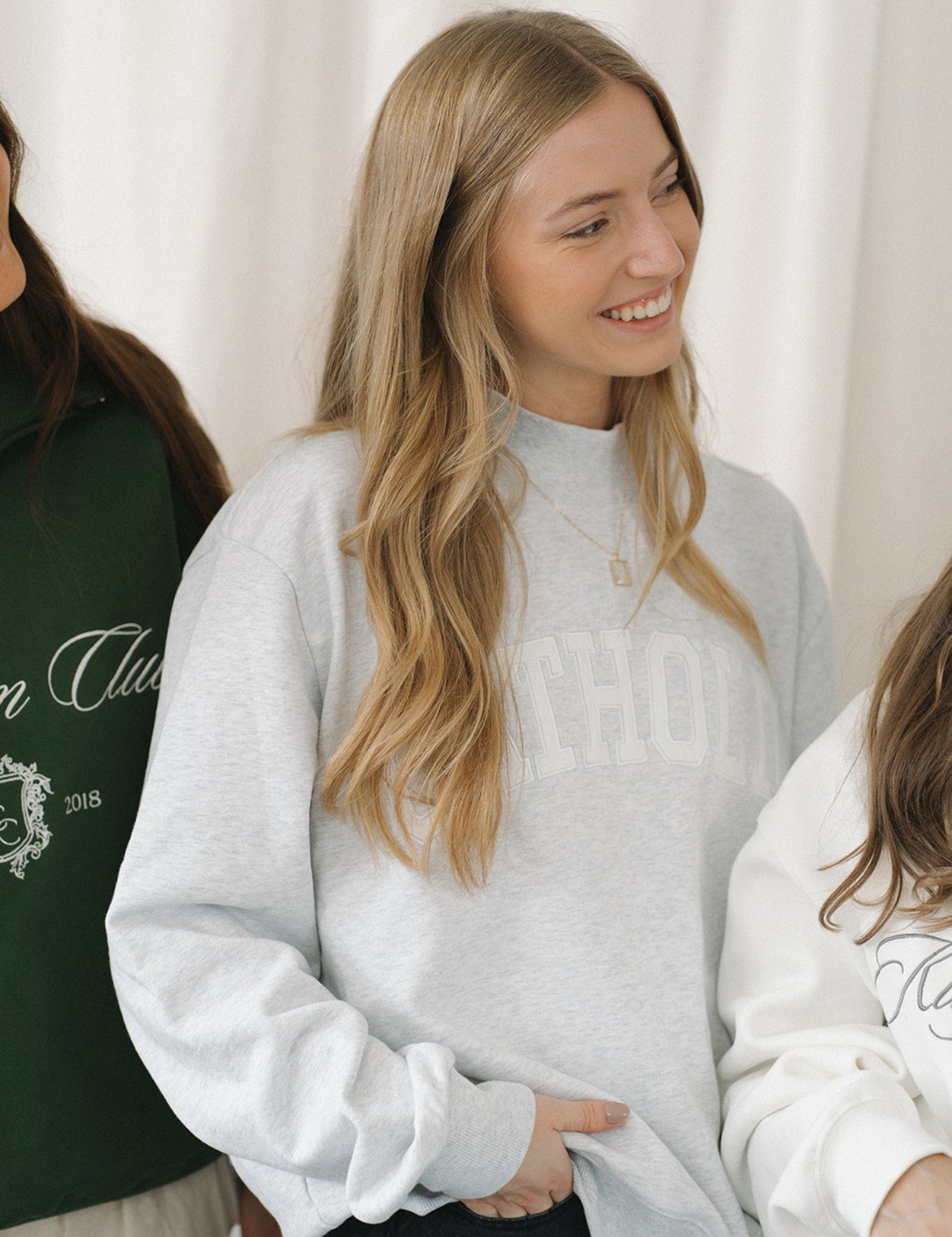 Woman wearing a light gray mockneck sweatshirt with a blurred background
