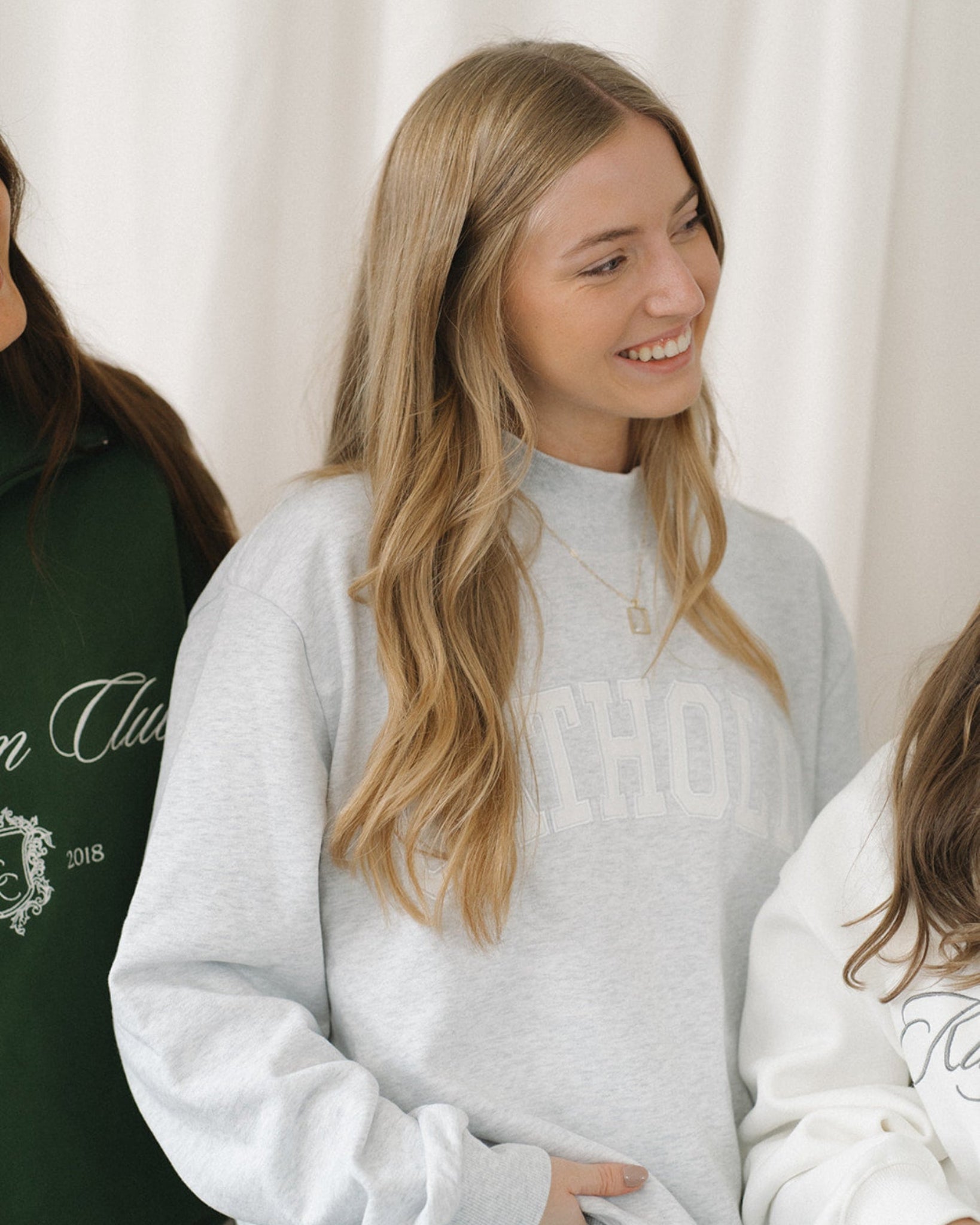Woman wearing a light gray mockneck sweatshirt with a blurred background