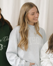 Woman wearing a light gray mockneck sweatshirt with a blurred background