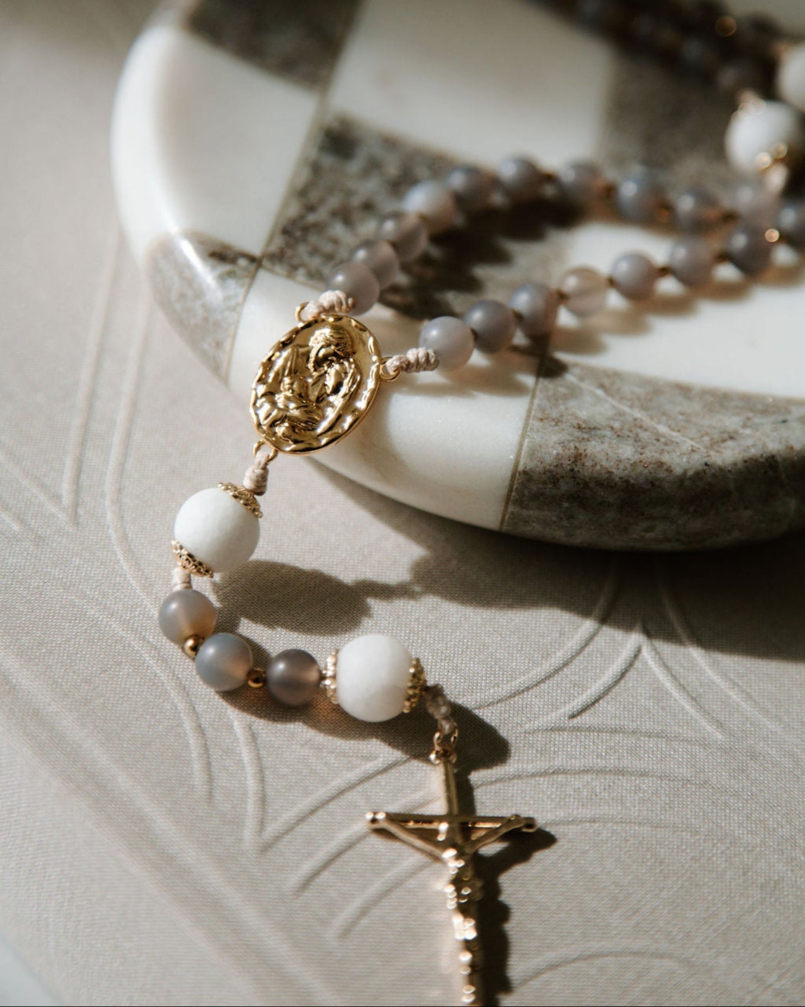 Durable catholic rosary with gold and white beads on a textured coffee table book.