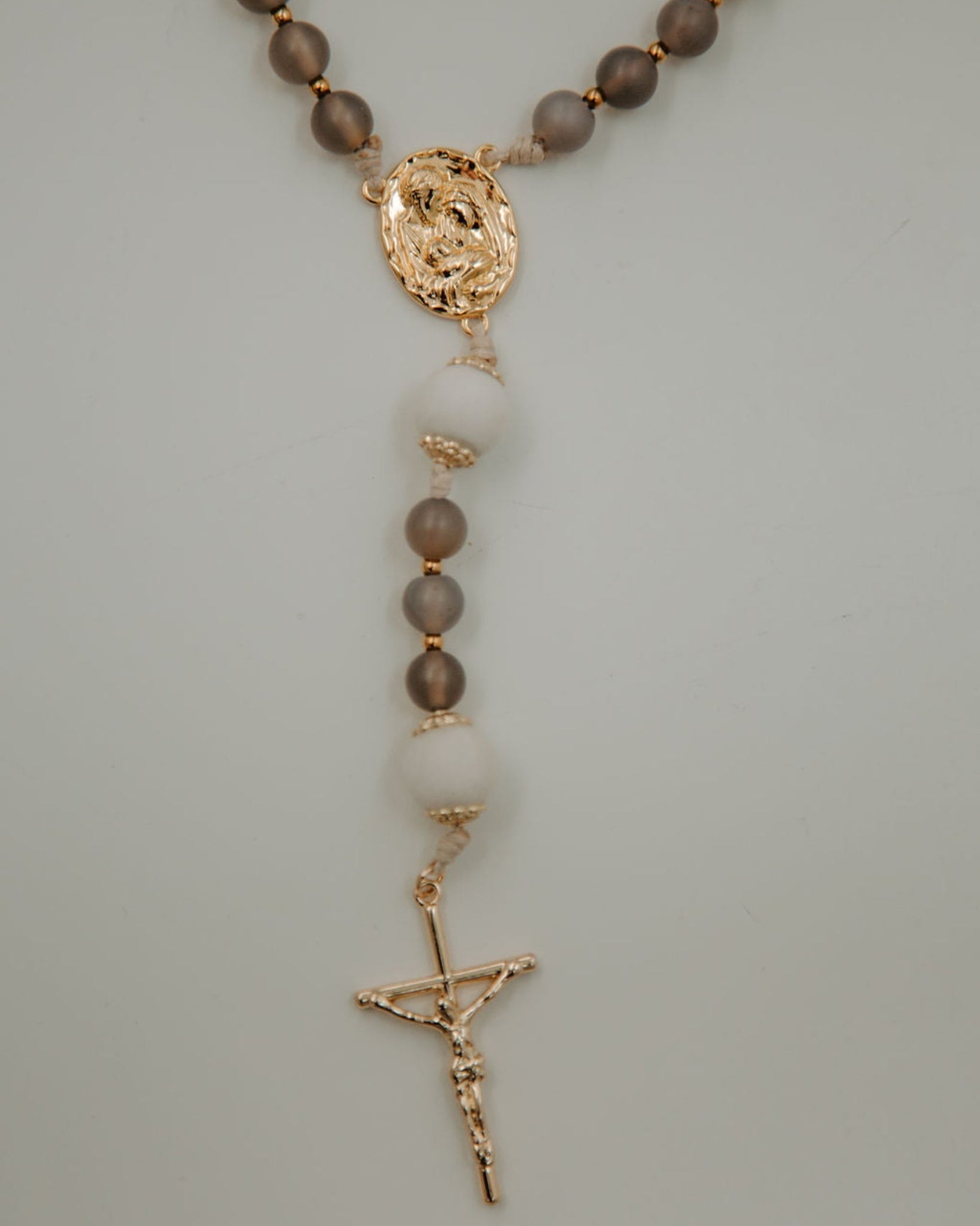 Holy Family Catholic rosary with brown and white beads and gold accents on a light gray background