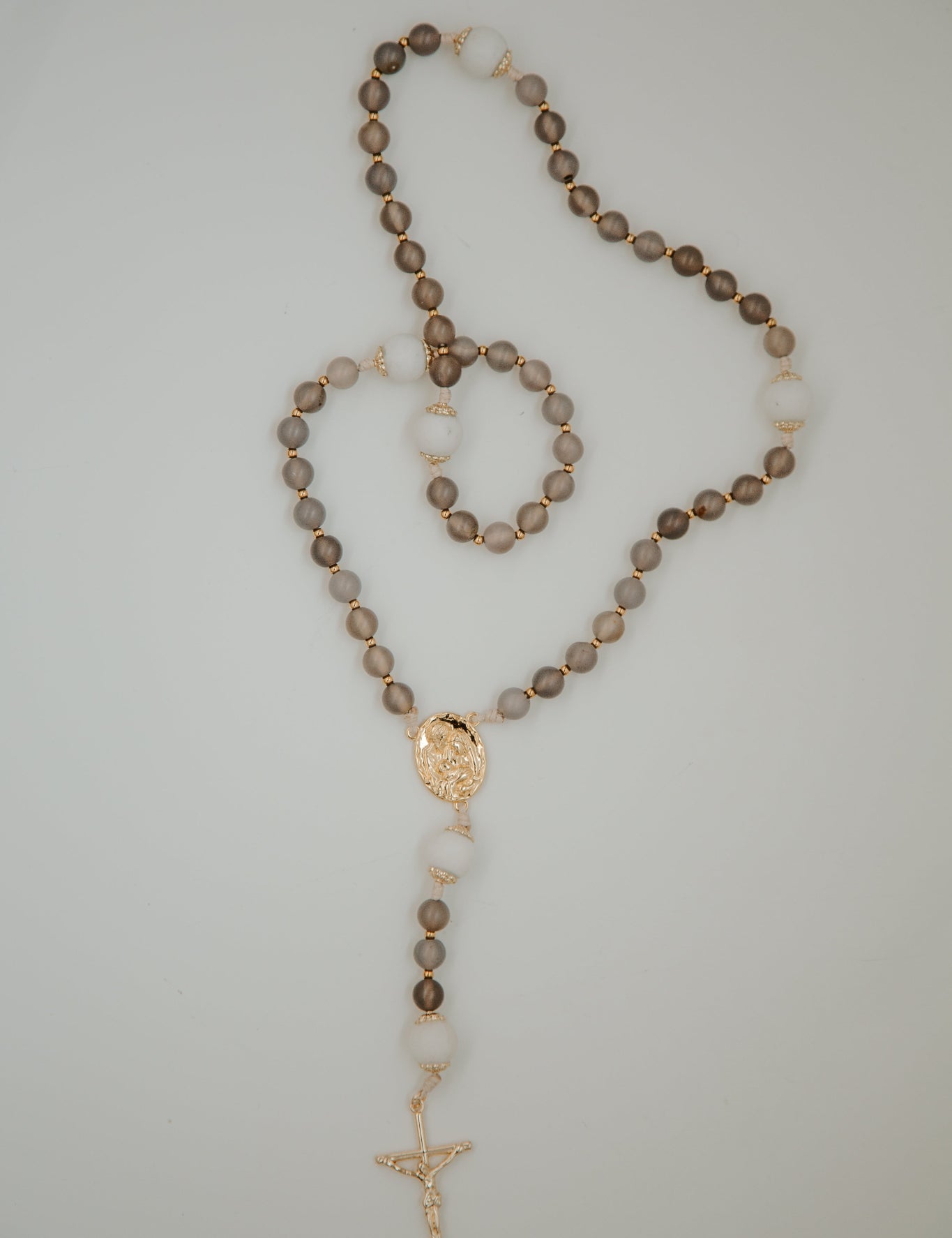 Rosary with brown beads and gold accents on a light gray background