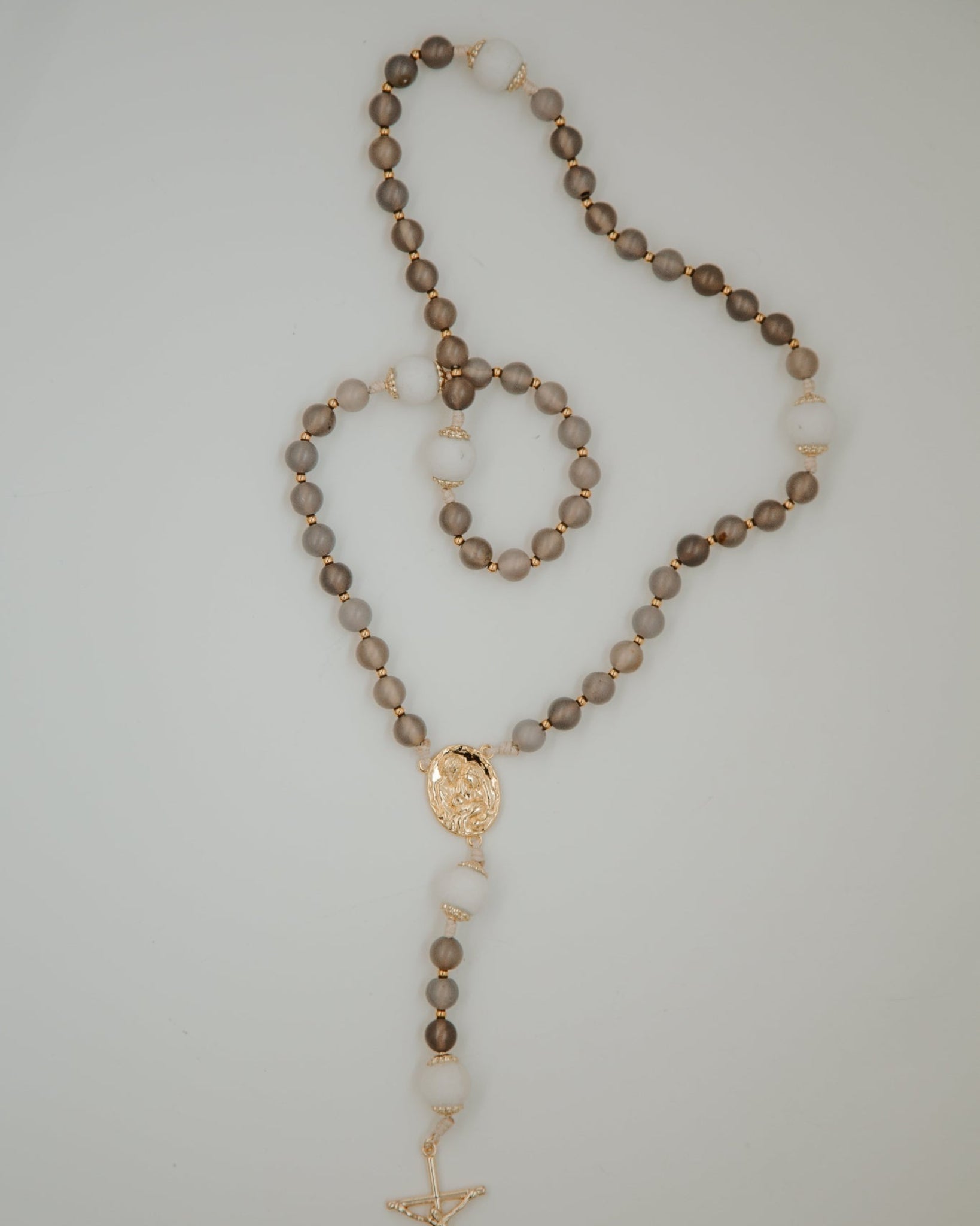 Rosary with brown beads and gold accents on a light gray background