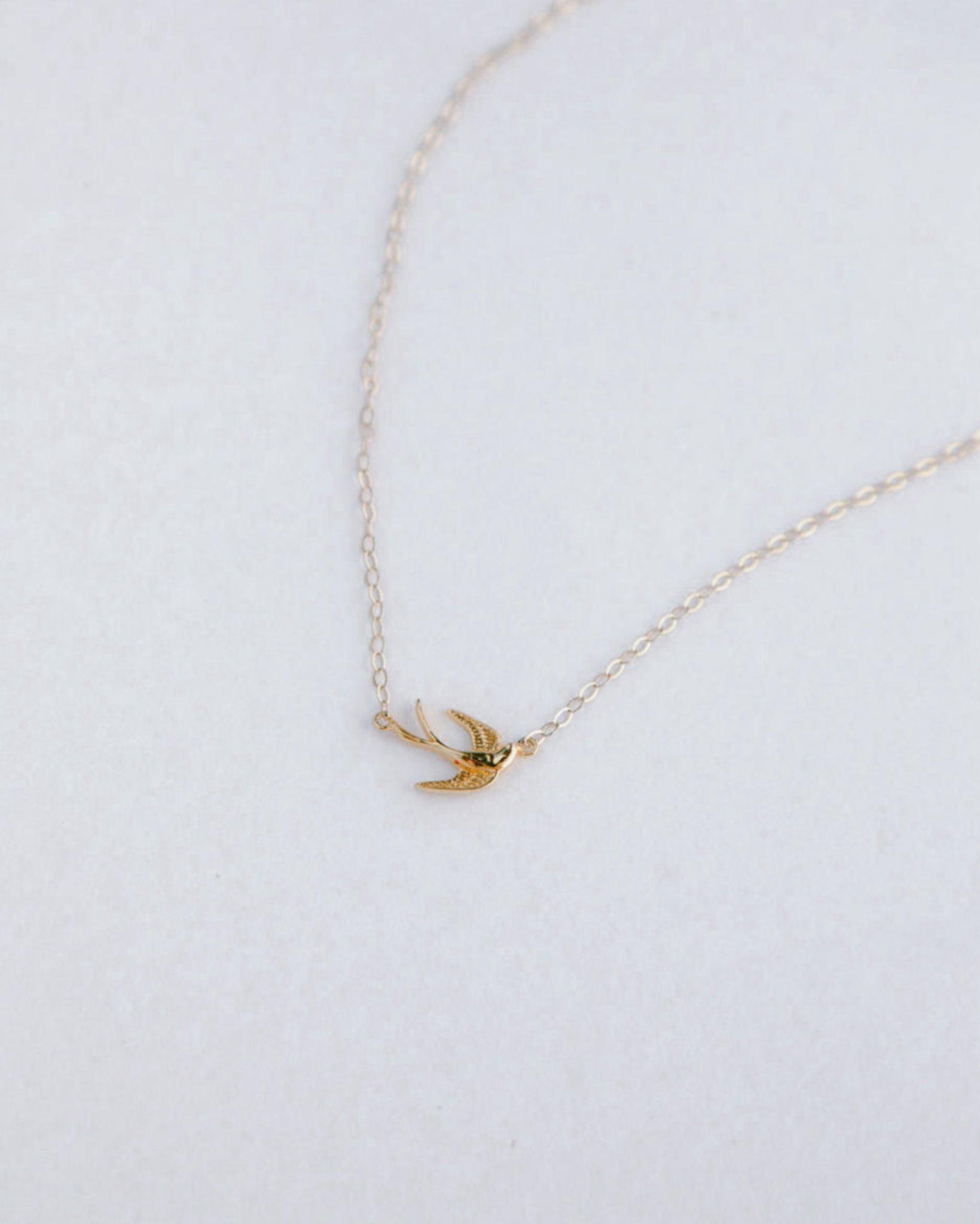 Gold holy spirit pendant on a thin chain against a light gray background