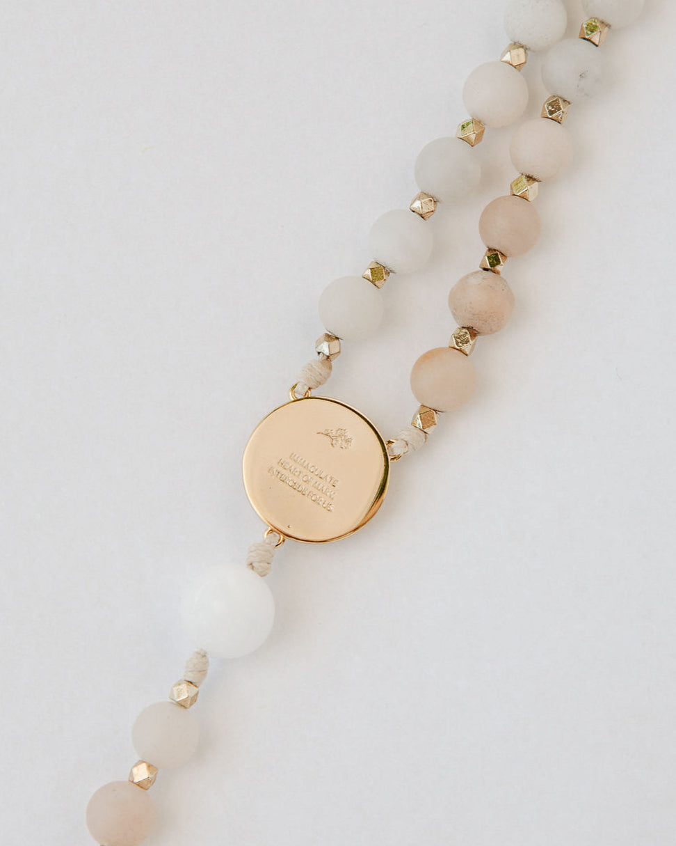 Pink and white immaculate heart rosary with gold medal on white background