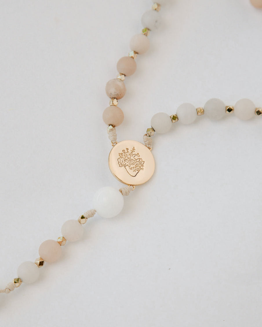 Pink and white immaculate heart rosary with gold medal on white background