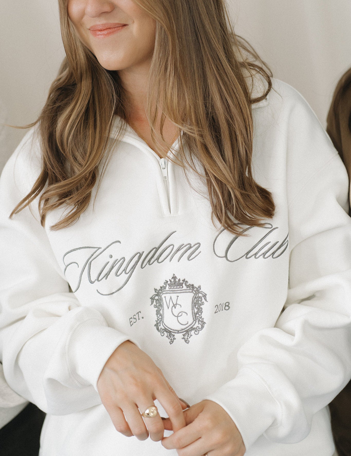 Person wearing a white hoodie with 'Kingdom Club' text and design.