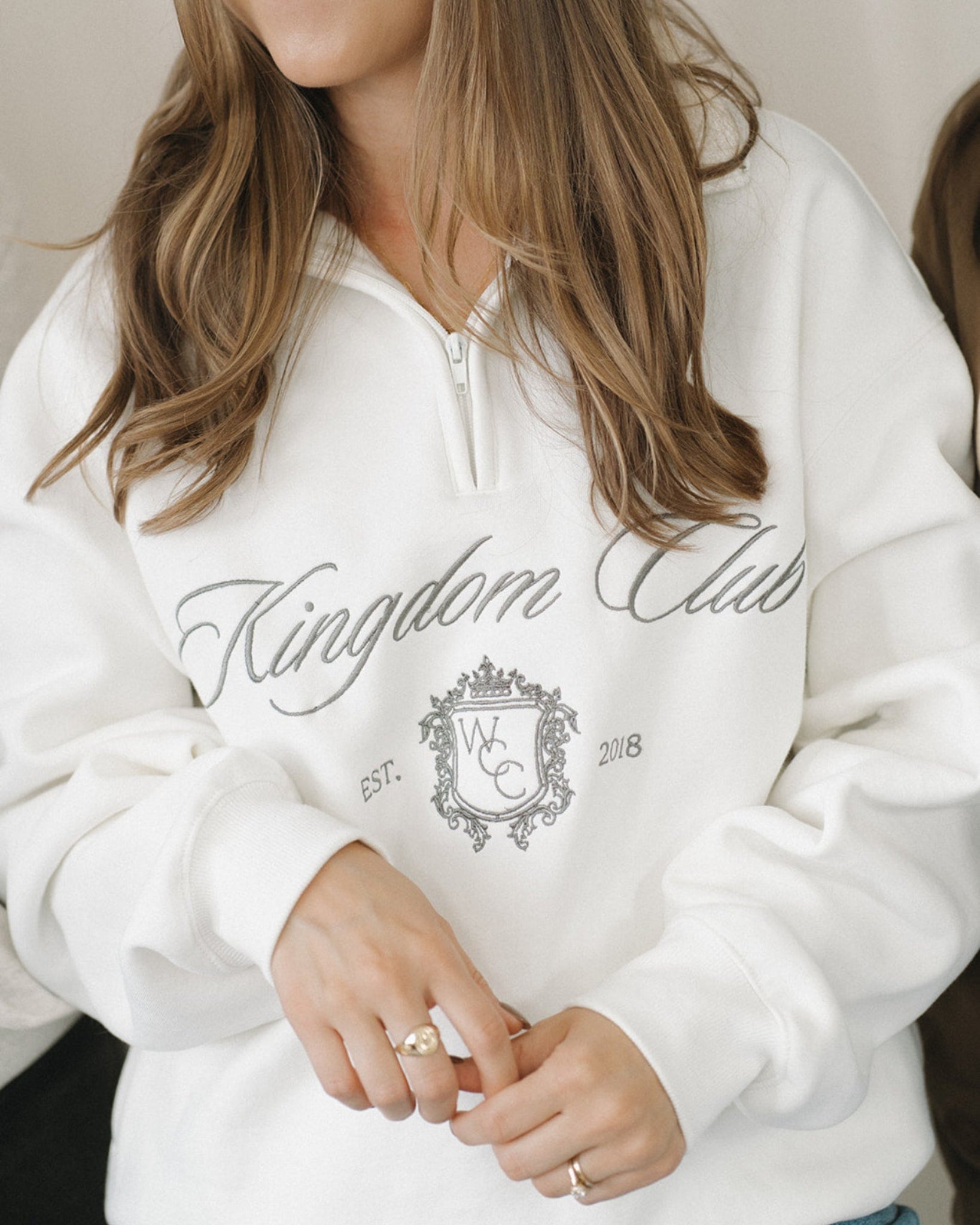 Person wearing a white hoodie with 'Kingdom Club' text and design.