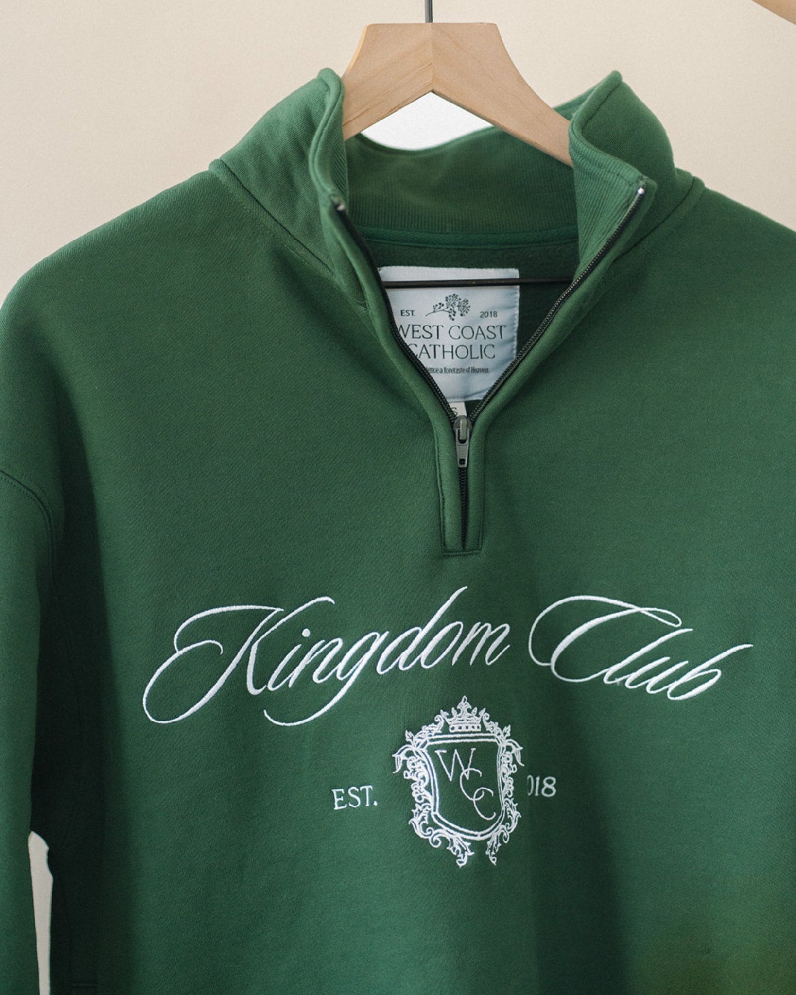 Green sweatshirt with 'Kingdom Club' text and logo on a hanger against a beige background