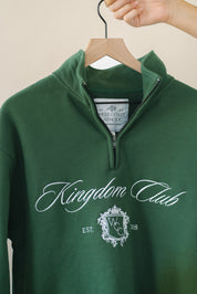 Green sweatshirt with 'Kingdom Club' text and logo on a hanger against a beige background