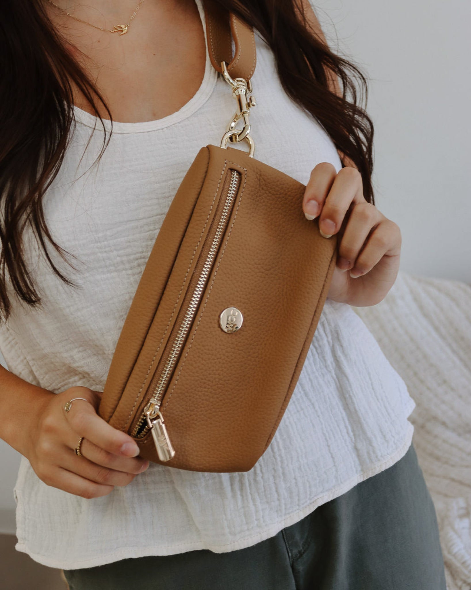Person holding a brown leather pouch with a gold zipper.