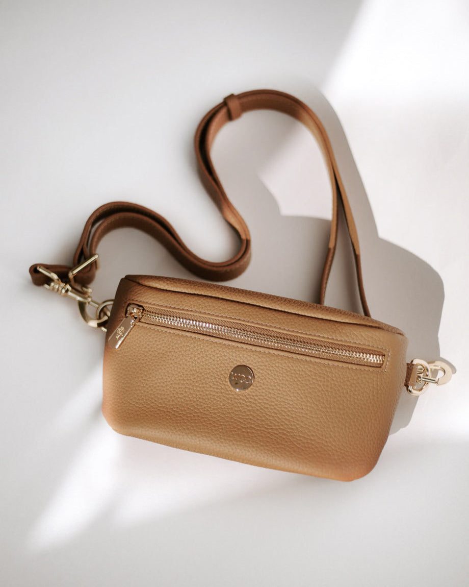 Tan leather crossbody bag with gold accents on a light background
