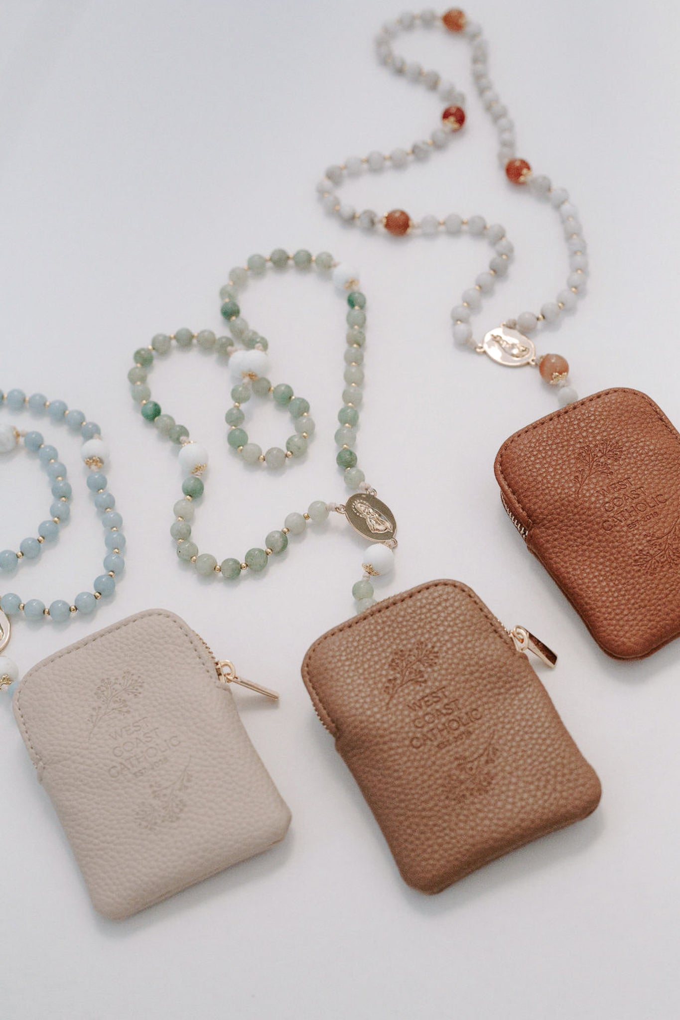 Three leather pouches in beige, brown, and brown with rosaries on a light gray background