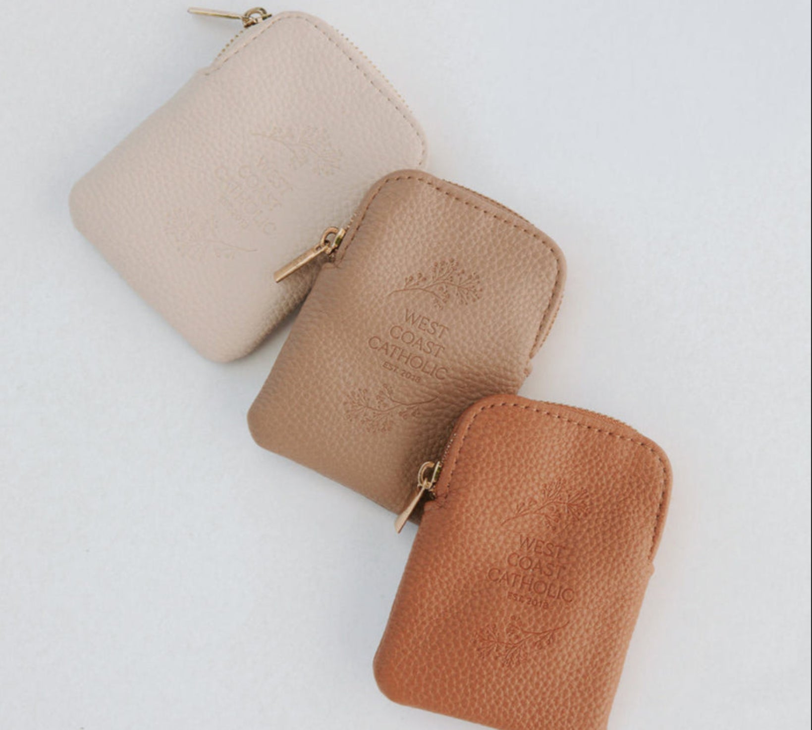 Three small leather pouches in beige, brown, and rust on a light gray background