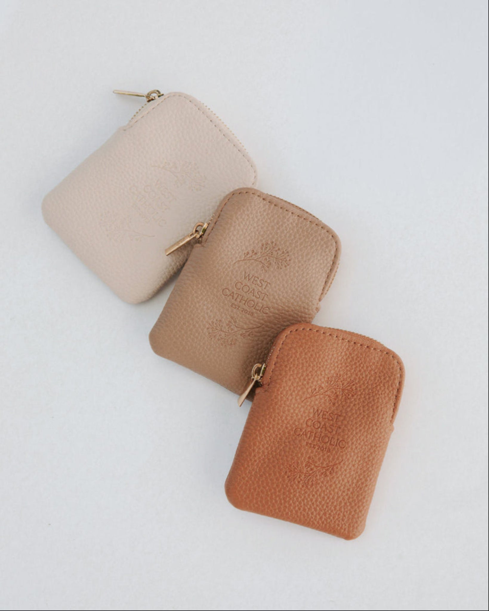 Three small leather pouches in beige, brown, and rust on a light gray background