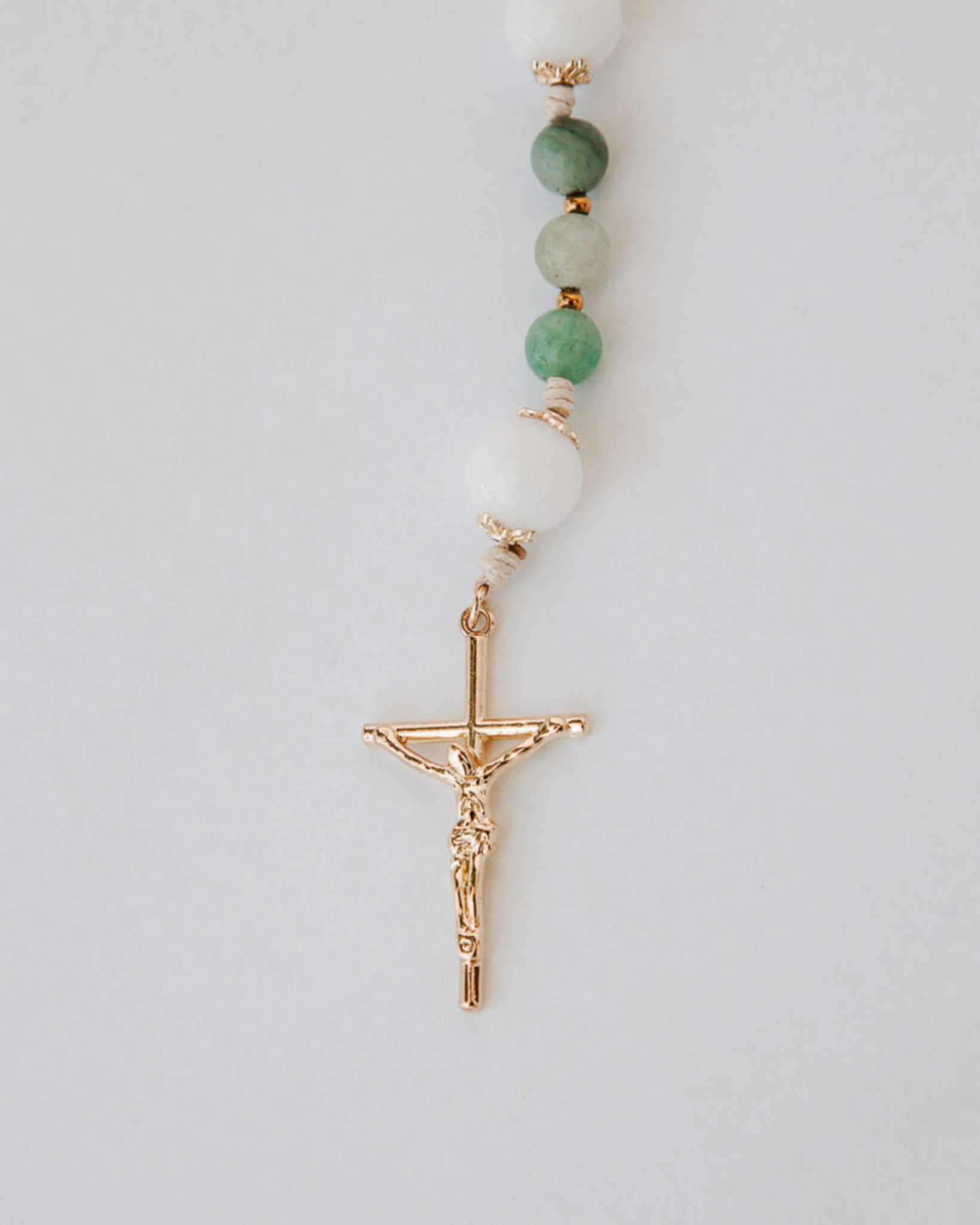 Beaded gemstone rosary with a gold cross pendant on a light gray background