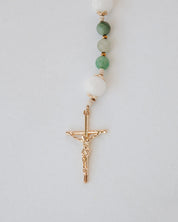 Beaded gemstone rosary with a gold cross pendant on a light gray background