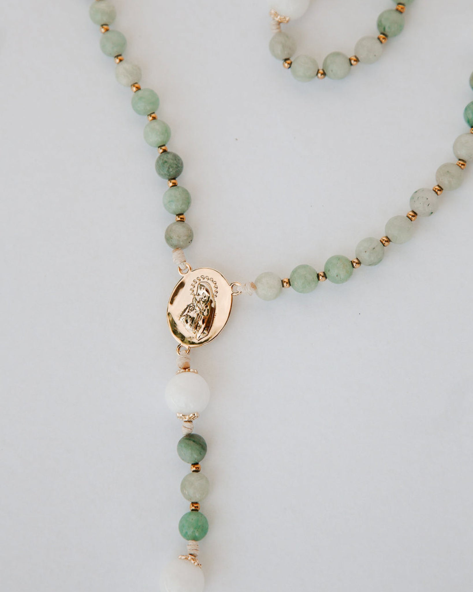 Beaded gemstone rosary with a gold pendant on a light gray background