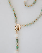 Beaded gemstone rosary with a gold pendant on a light gray background