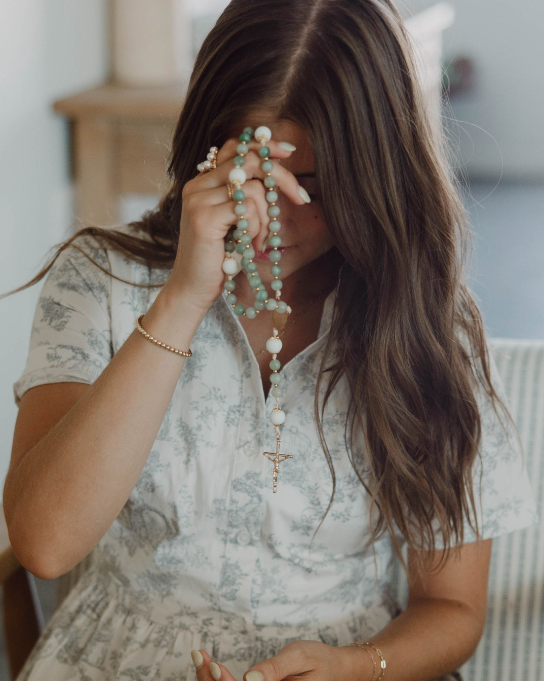 Woman praying with lourdes rosary in a casual indoor setting