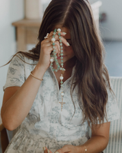Woman praying with lourdes rosary in a casual indoor setting