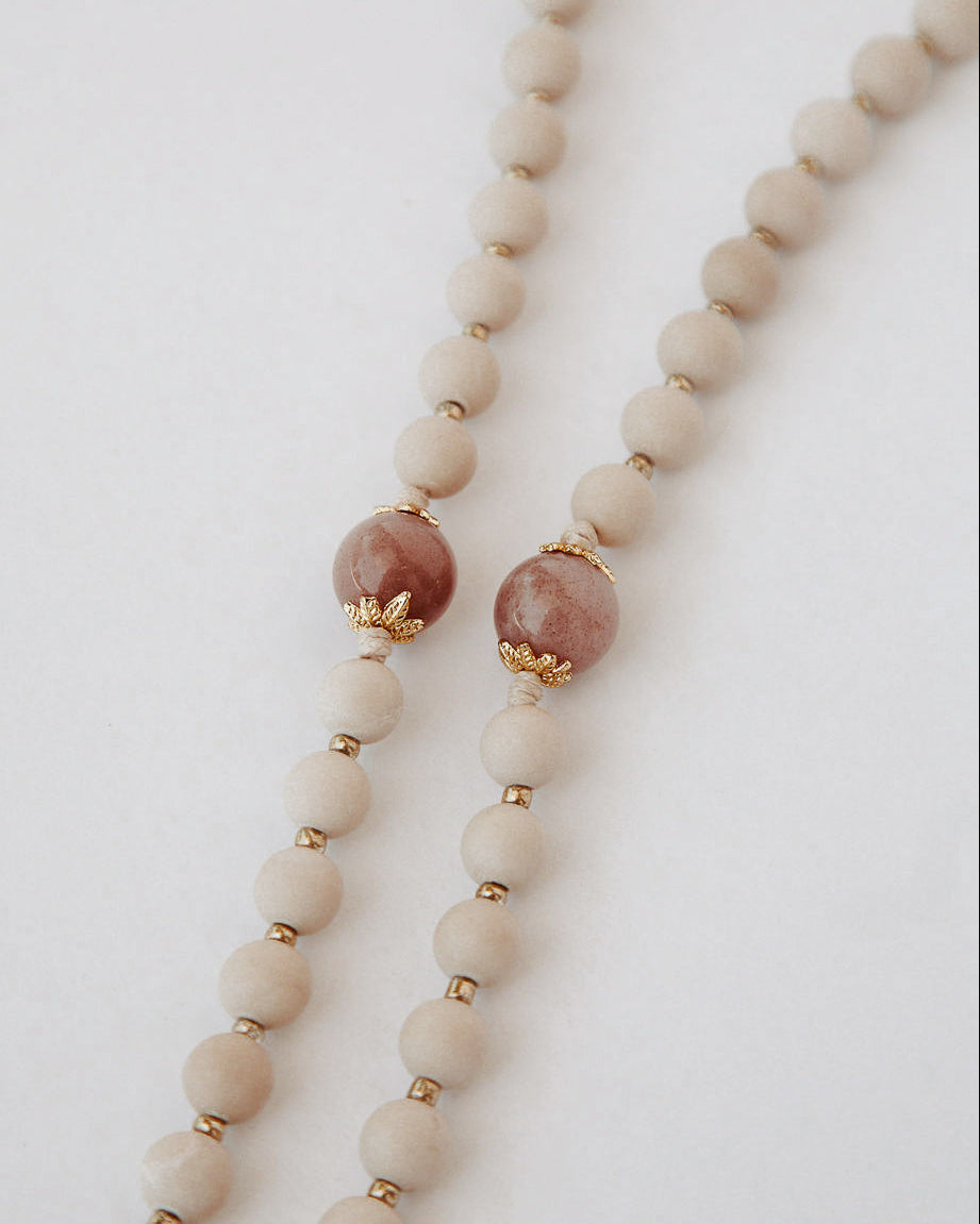 Close up of madonna rosary beads with beige and pink on a light background