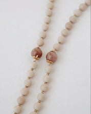 Close up of madonna rosary beads with beige and pink on a light background