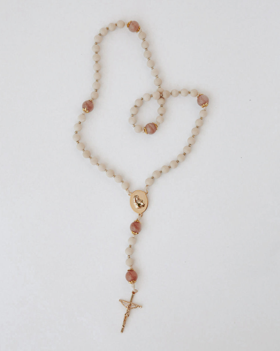Rosary with beige and pink beads and a gold details on a light background
