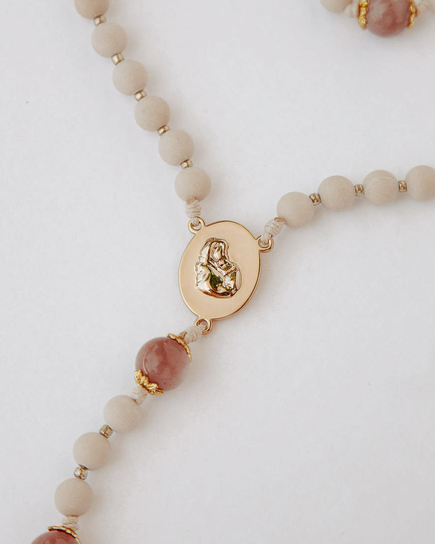 Close up of gold rosary medal with beige and pink beads on white background