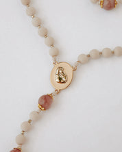 Close up of gold rosary medal with beige and pink beads on white background